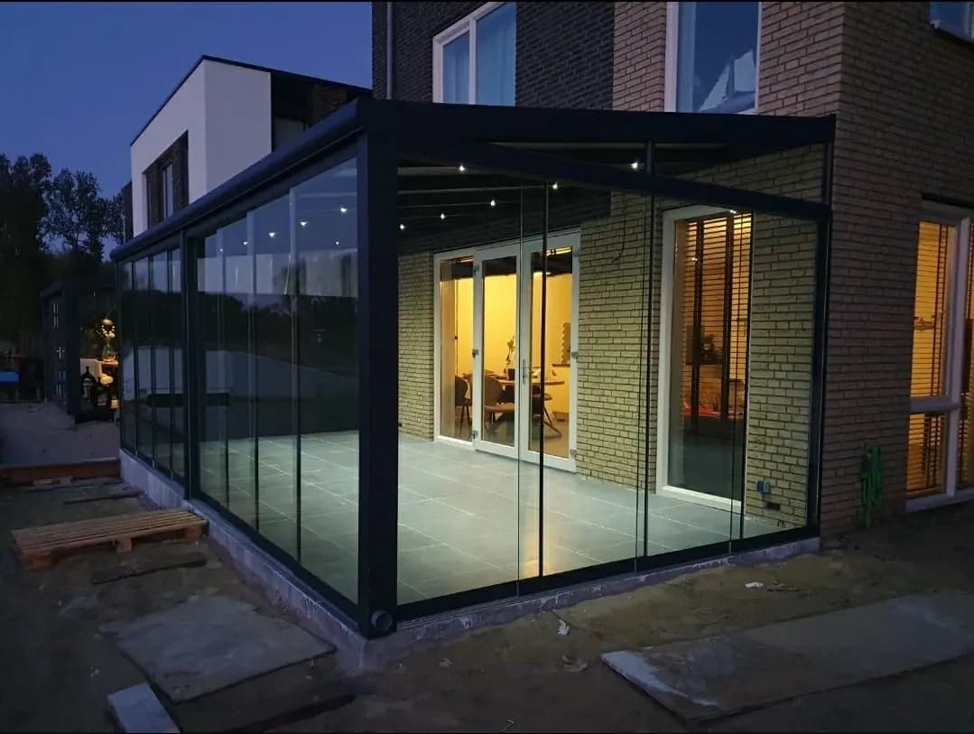 Glazen veranda aan een woning in de avond, met spots in het dak